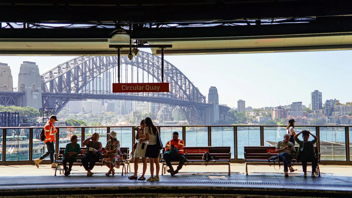 Commuters waiting on a Sydney train station platform near the Harbour Bridge
