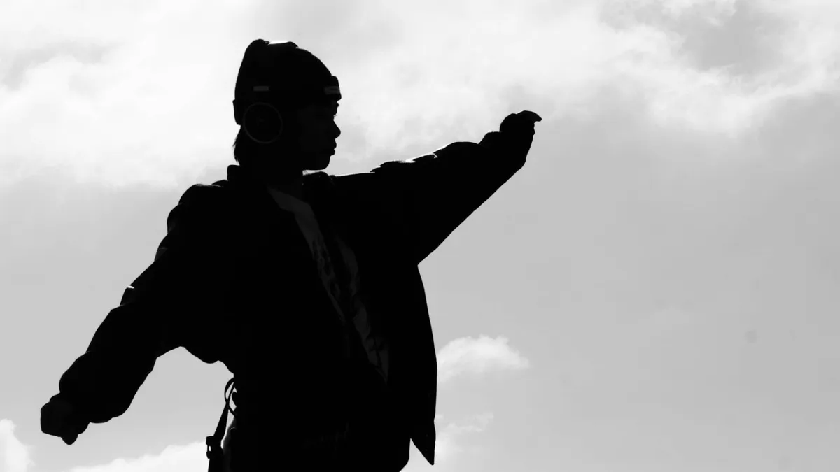 Silhouette of a man holding out his arm against a pale sky