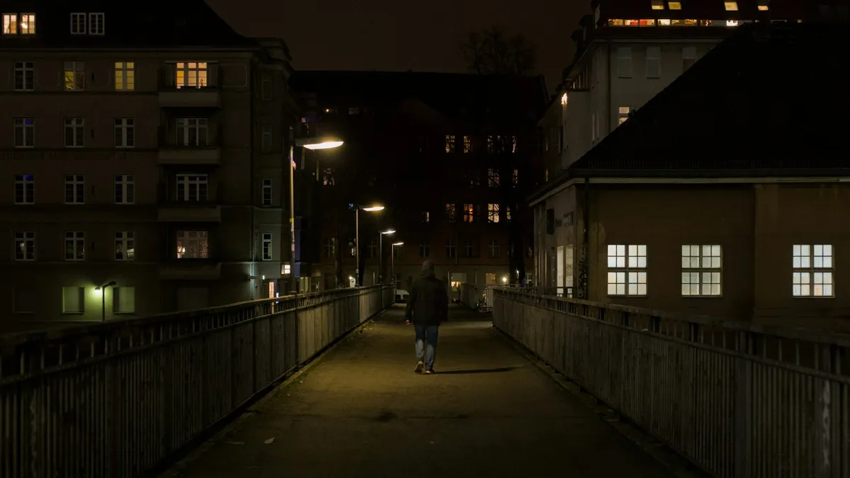 Person walking alone across a bridge at night